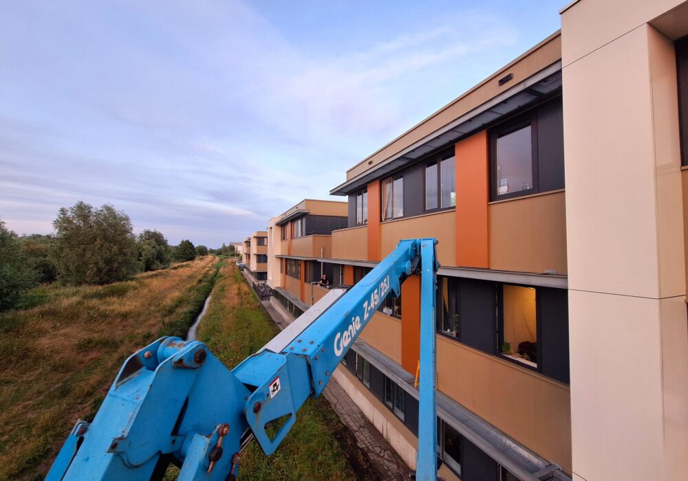 Hoogwerker langs de gevel van een appartementencomplex tijdens gevelreiniging