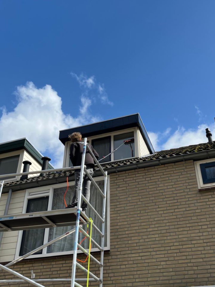 Medewerker van Burm & Co reinigt een dakkapel en de boeidelen vanaf een steiger
