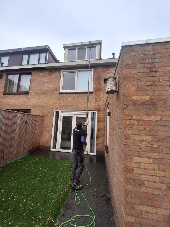 Medewerker van Burm & Co reinigt een dakkapel aan de achterkant van een woning met een telescoopsteel