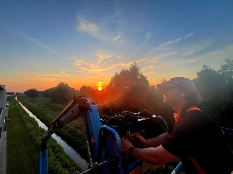 Burm & Co aan het werk in de hoogwerker bij zonsondergang