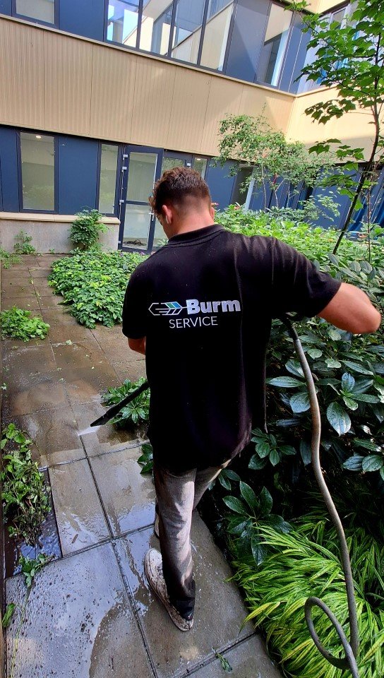 Medewerker van Burm & Co spuit een tegelpad met groene aanslag schoon