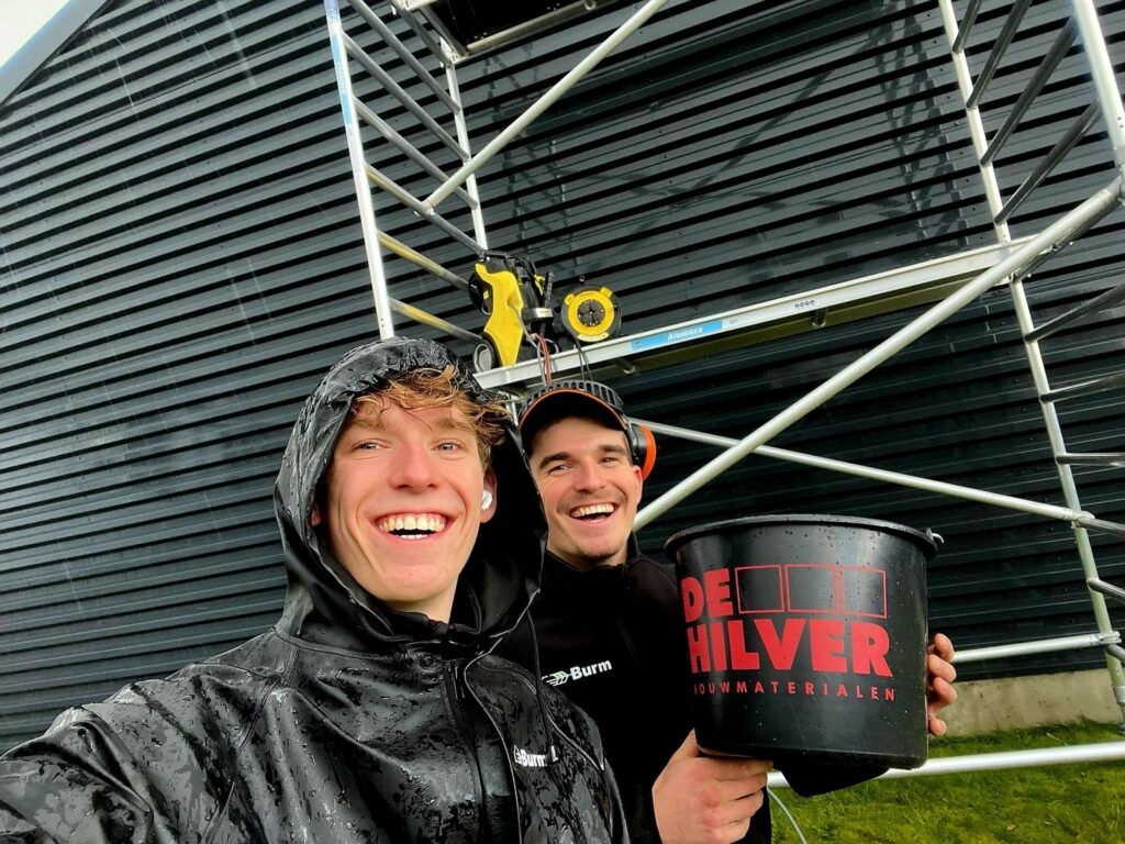 Burm & Co bij de rolsteiger op het terrein van Roozen van Hoppe, met een emmer van De Hilver Bouwmaterialen